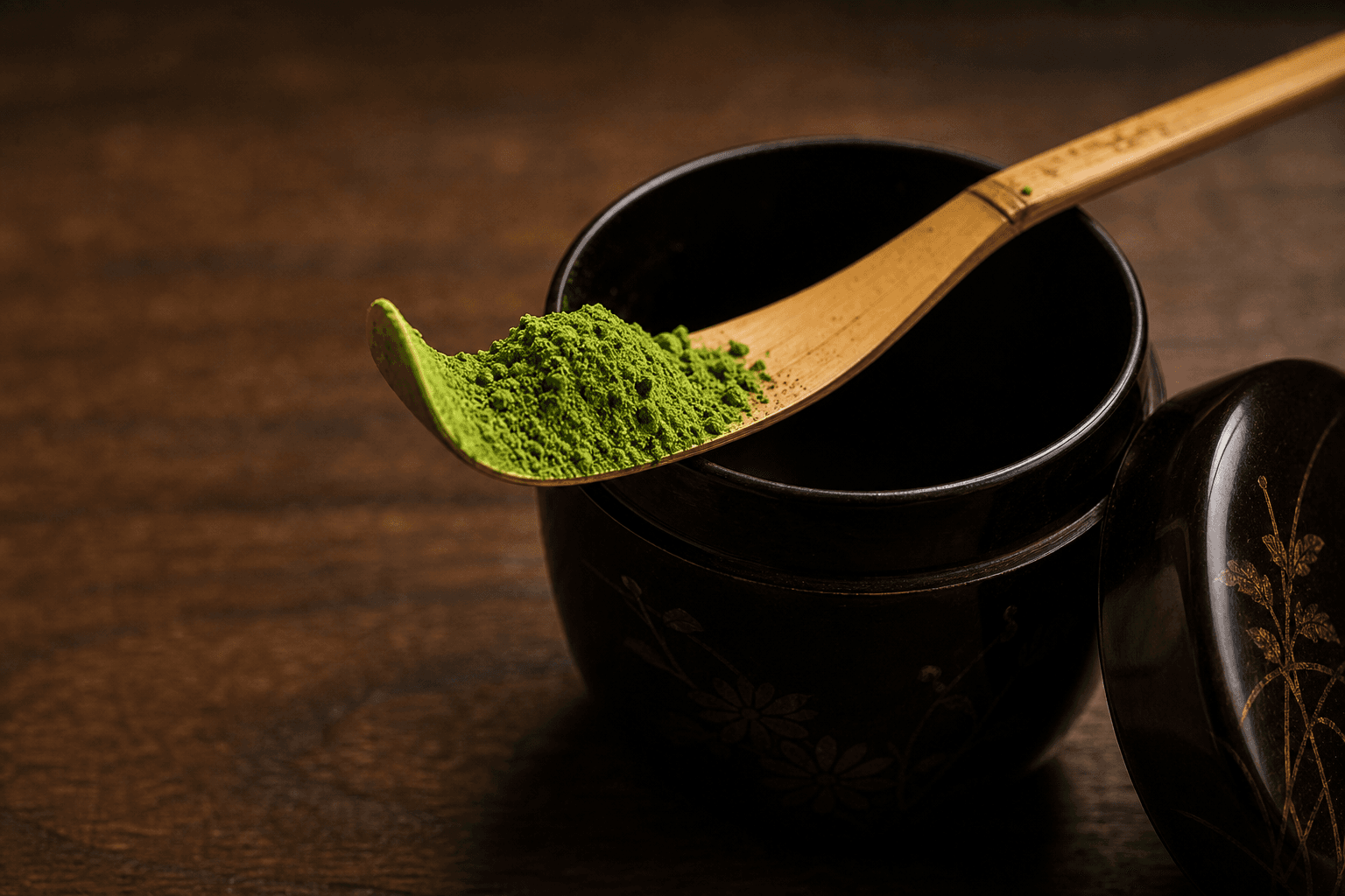 A bamboo chashaku heaped with matcha powder resting across a lacquer tea caddy